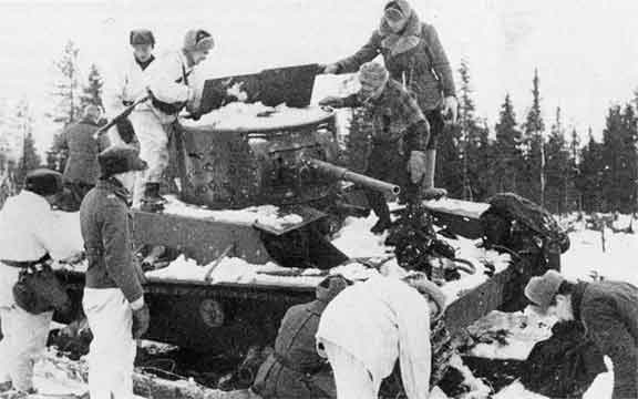 Finnish soldiers, some in snow camouflage, inspecting an abondoned Soviet T-26 tank after the Battle of Raate road during the Winter War.