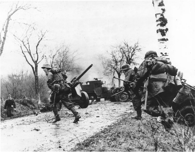 German troops advancing past abandoned American equipment. Battle of the Bulge, 1944