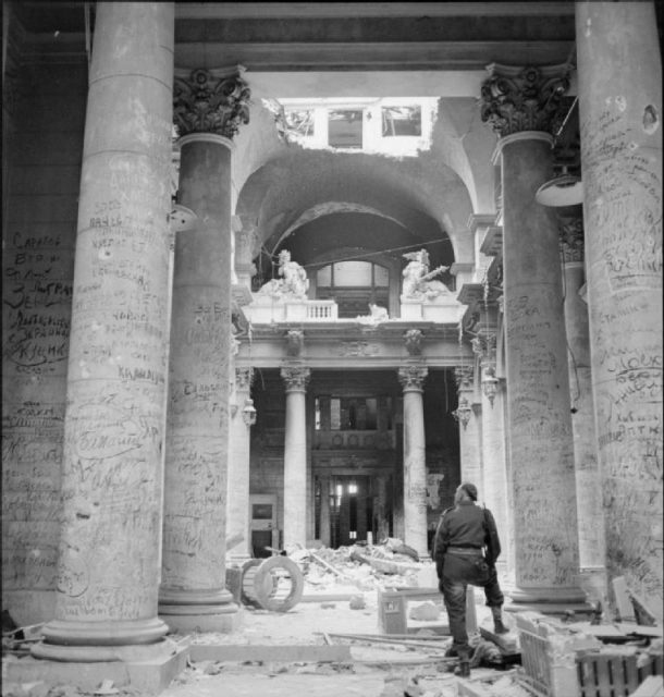 On 3 July 1945, graffiti left by Soviet soldiers covers the pillars inside the ruins of the German Reichstag building in Berlin. A British soldier is standing among the ruins and looking at the pillars.