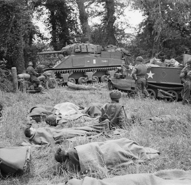 The British Army in Normandy 1944 A Sherman tank and Universal carrier wait to advance. Note wounded resting under blankets in the foreground.