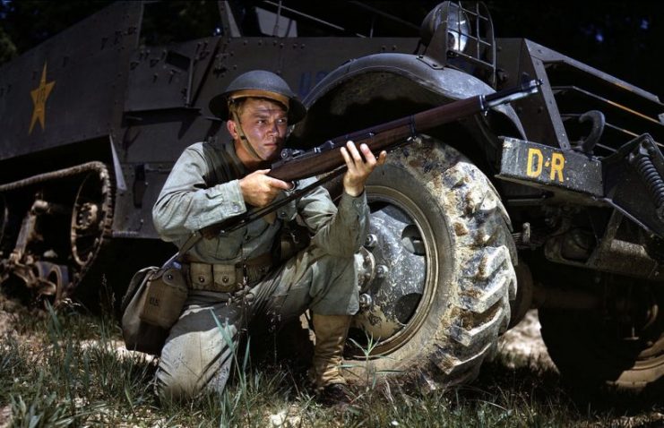 World War II Infantryman, kneeling in front of M3 Half-track, holds and sights an M1 Garand rifle. Fort Knox, Kentucky, June 1942.