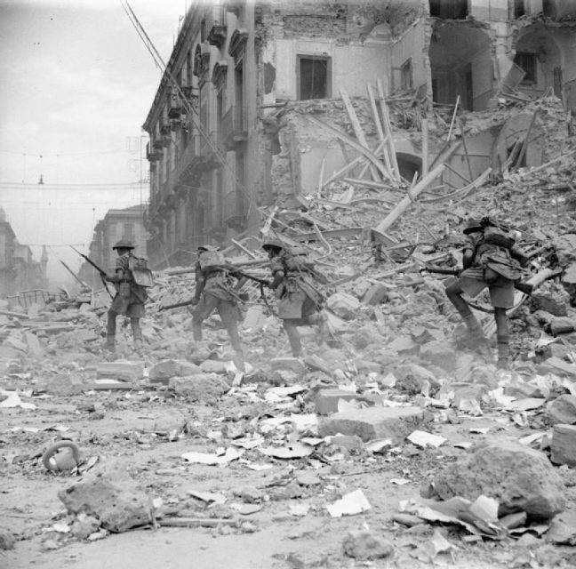 British troops scramble over rubble in a devastated street in Catania, Sicily, 5 Aug 1943. (Operation Husky)