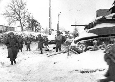 Members of the 117th Infantry Regiment, 30th Infantry Division, move past a destroyed American M5 “Stuart” tank on their march to capture the town of St. Vith at the close of the Battle of the Bulge