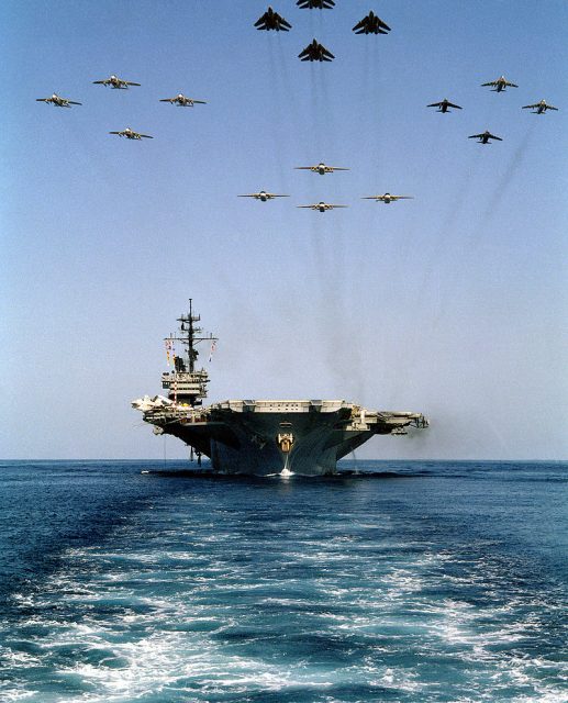 A bow view of the aircraft carrier USS AMERICA (CV-66) underway as 16 aircraft from Carrier Air Wing One (CVW-1) fly overhead.