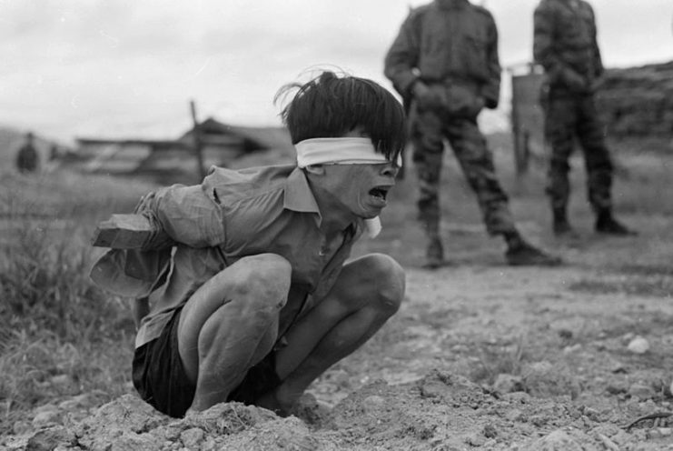 A suspected Viet Cong prisoner captured in 1967 by the U.S. Army awaits interrogation. He has been placed in a stress position by tying a board between his arms.