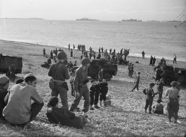 British sailors and British and American soldiers on the beach near Algiers. A 40 mm Bofors gun can be seen further down the beach along with three lorries.