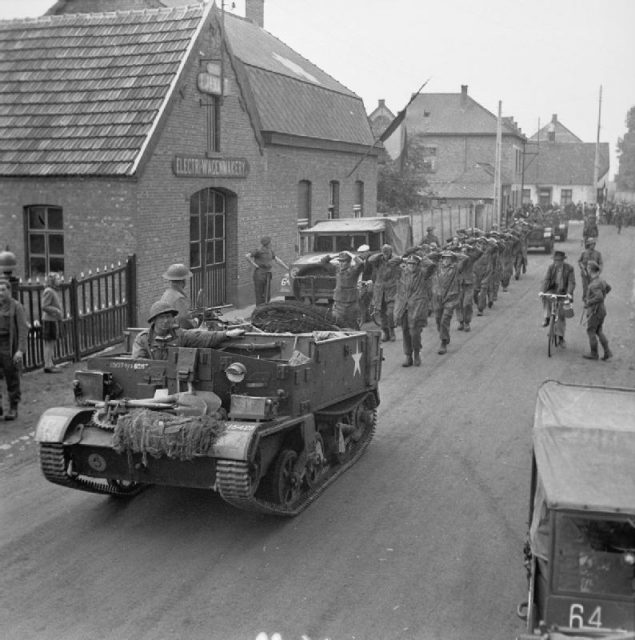 A British Army Universal Carrier leads some German prisoners-of-war into a European town.