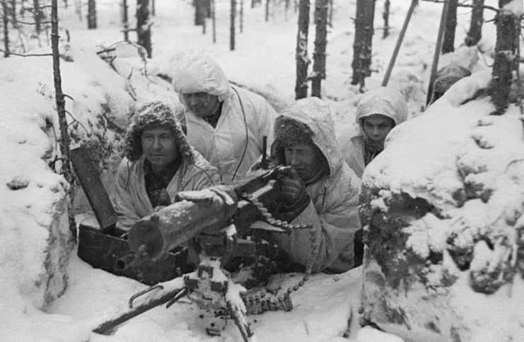 A group of Finnish soldiers in snowsuits manning a heavy machine gun in a foxhole.