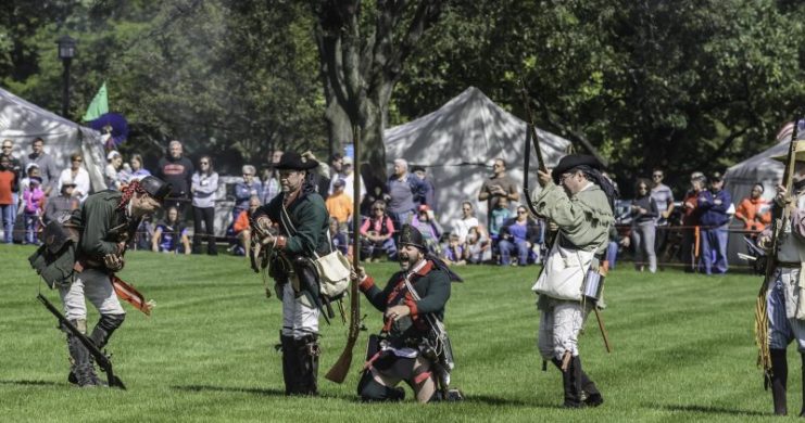 Two soldiers, one about to fall and one on his knees, pretend to have been shot during a mock battle at a reenactment of the American Revolutionary War (1775-1783).