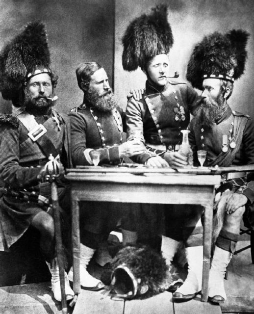 Photograph of Piper David Muir, George Glen, Donald McKenzie and Colour Sergeant William Gardner, 42nd Royal Highlanders, posed grouped round a table with drinks at Aldershot, UK.