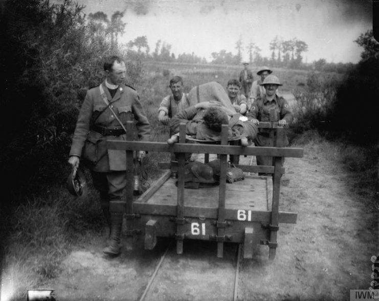 A wounded man on a stretcher is put back on to the trolley to be taken to the rear. By the side of the trolley walks a military chaplain. Near Kemmel, June 10, 1917.