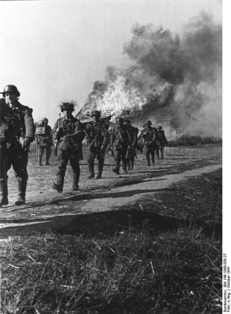 German soldiers march by a burning home in Soviet Ukraine, October 1941.Bundesarchiv, Bild 146-1989-030-27 / CC-BY-SA 3.0
