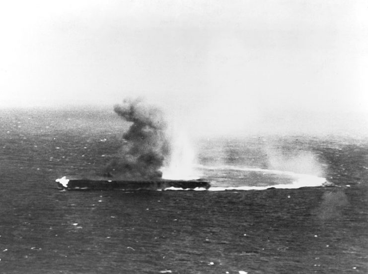 Shōkaku, at high speed and turning hard, has suffered bomb strikes and is afire.