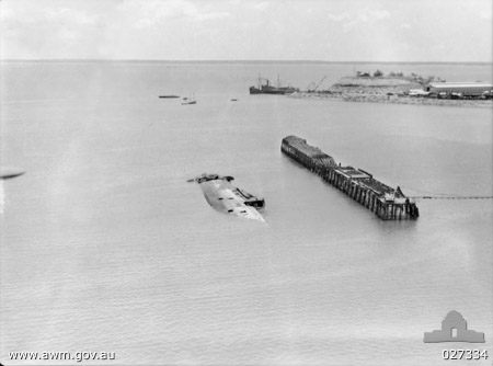 A sunken ship (MV Neptuna) and burnt-out wharf in Darwin Harbour following the attack (AWM 027334)