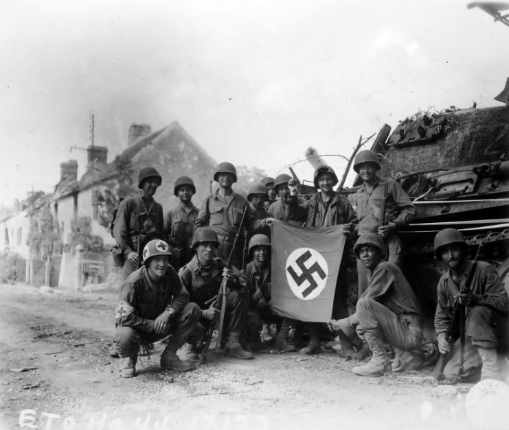 US soldiers celebrate with a captured German flag in front of a destroyed Panther tank. The group of infantrymen were left behind to “mop-up” in Chambois, France, last stronghold of the Germans in the Falaise Gap area.