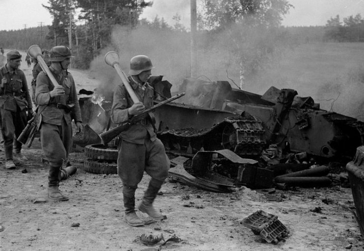 Finnish soldiers carrying Panzerfäuste on their shoulders pass by the remains of a destroyed Soviet T-34 tank
