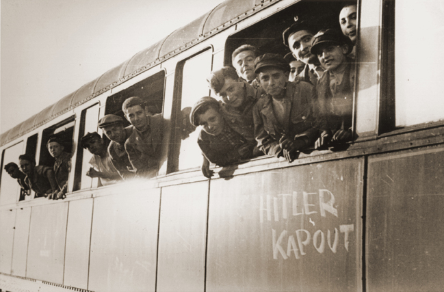 Jewish youth liberated at Buchenwald lean out the windows of a train, as it pulls away from the station. The train, which has been marked with the phrase “Hitler kaput” (“Hitler is finished” in several European languages), will transport the children to an OSE home in Ecouis, France.