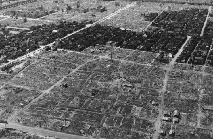 A view of Tokyo, Japan after the war in 1945. A strip of undamaged residential buildings surrounded by ashes and rubble of neighboring structures burned to the ground.