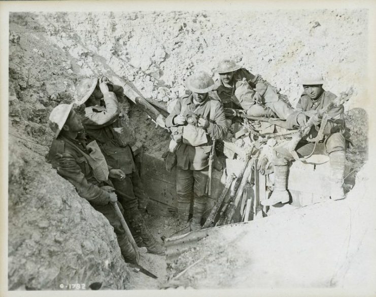 Canadian soldiers in captured German trench during the Battle of Hill 70 in August 1917. The soldiers on the left are scanning the sky for aircraft, while the soldier in the center appears to be re-packing his gas respirator into the carrying pouch on his chest. Dust cakes their clothes, helmets, and weapons.