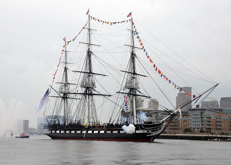 Constitution, dressed overall, fires a 17-gun salute in Boston Harbor, 4 July 2014