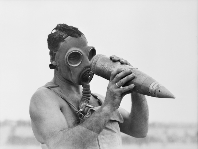 An observer who has moved into a gas-affected target area to record results, examines an un-exploded shell.
