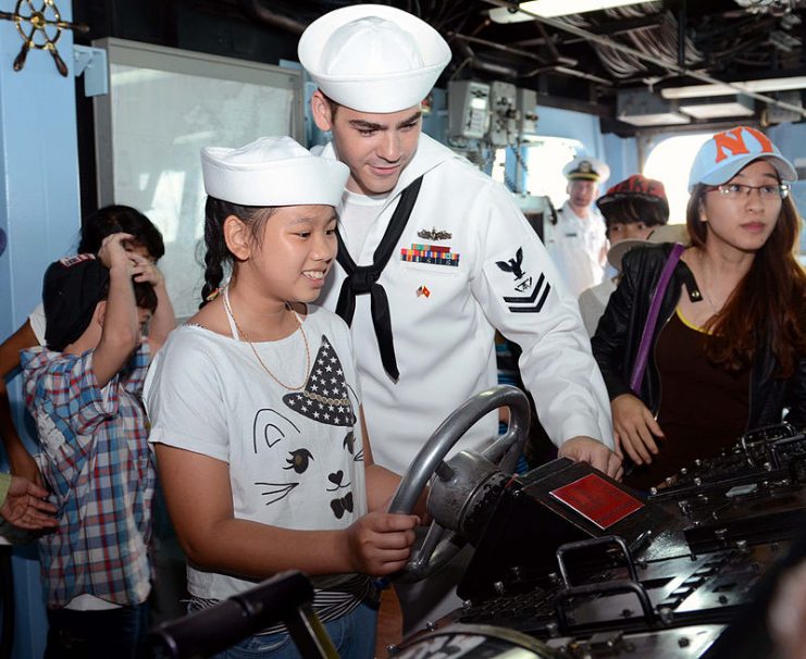 A US Navy sailor shows a child how to steer the Arleigh Burke-class destroyer USS John S. McCain (DDG 56) during a shipboard tour.