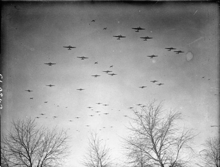 Douglas Dakotas of No. 46 Group fly in formation over Wavre, Belgium, heading for the dropping zones east of the River Rhine. Above them, Dakotas towing Airspeed Horsas fly a divergent course towards their objectives.