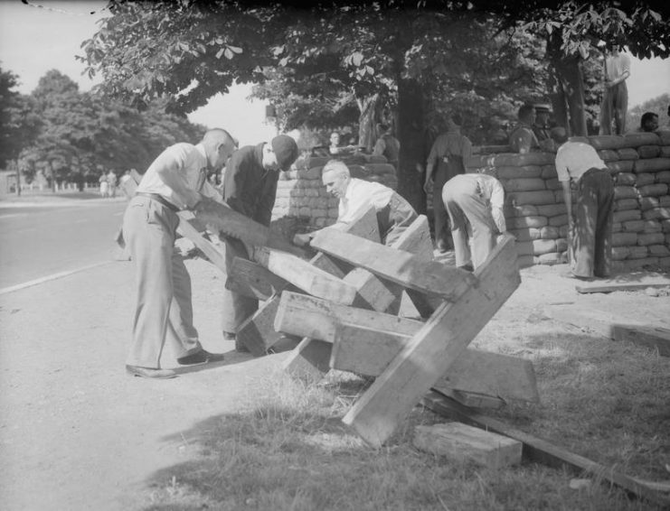 Members of the Local Defence Volunteers (LDV) construct wooden road barricades and a sandbagged defence post at Woodford Wells, Essex, 1 July 1940.
