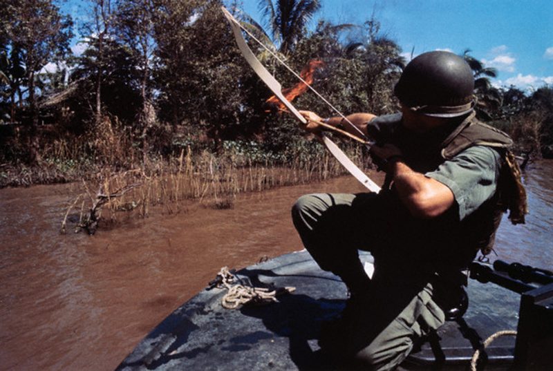 08 Dec 1967, Bassac River, South Vietnam --- A Navy lieutenant aims his flaming arrow at a hut across the river that conceals a Viet Cong bunker. --- Image by © Bettmann/CORBIS