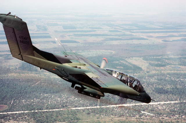 An air-to-air right side view of an OV-10 Bronco aircraft firing a white phosphorous smoke rocket to mark a ground target. The aircraft is used by forward air controllers in support of ground troops. Photo from November 84 Airman Magazine.