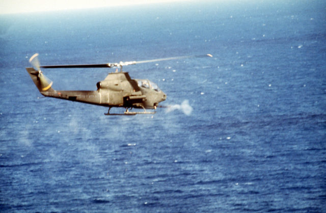 An air-to-air right side view of an AH-1 Cobra helicopter firing its 20mm cannon during a mission in support of Operation Urgent Fury.
