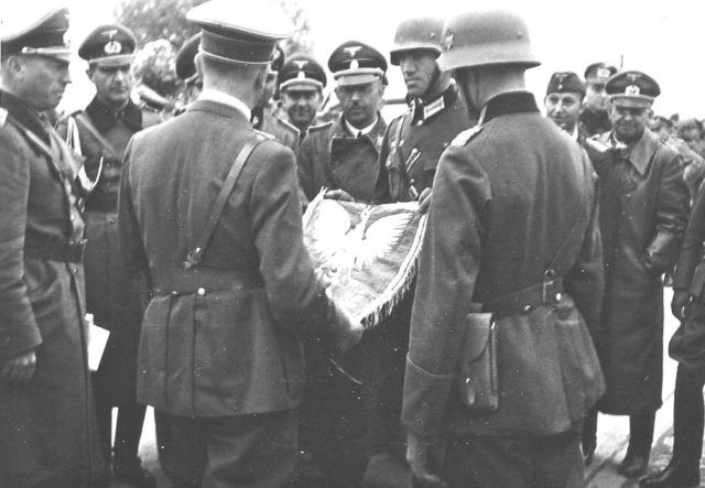 Himmler (behind flag) with Hitler (front left, back turned, holding flag) and Konrad Henlein (on the right) (Gauleiter Sudetenland) in Poland in September 1939 [B[By Picture from Josef Gierse, my dead uncle, I am the heir of the picture - Praca własna, CC BY 3.0, https://commons.wikimedia.org/w/index.php?curid=8340193]<figcaption class=