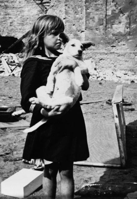 A girl holding her dog in a devastated neighborhood in Warsaw, Poland. 5 September 1939 [U[United States Holocaust Memorial Museum | Public Domain]<figcaption class=