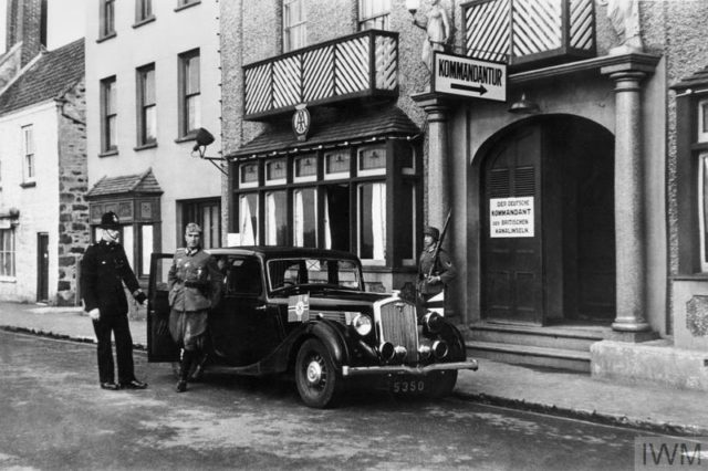A British policeman holds the door of a staff car as Major Albrecht Lanz, the first German Kommandant of Guernsey and Jersey, alights outside his Headquarters (Kommandantur) at the former Channel Islands Hotel on Glategny Esplanade, Saint Peter Port, Guernsey. Copyright: © IWM (HU 3616). Photo Credit