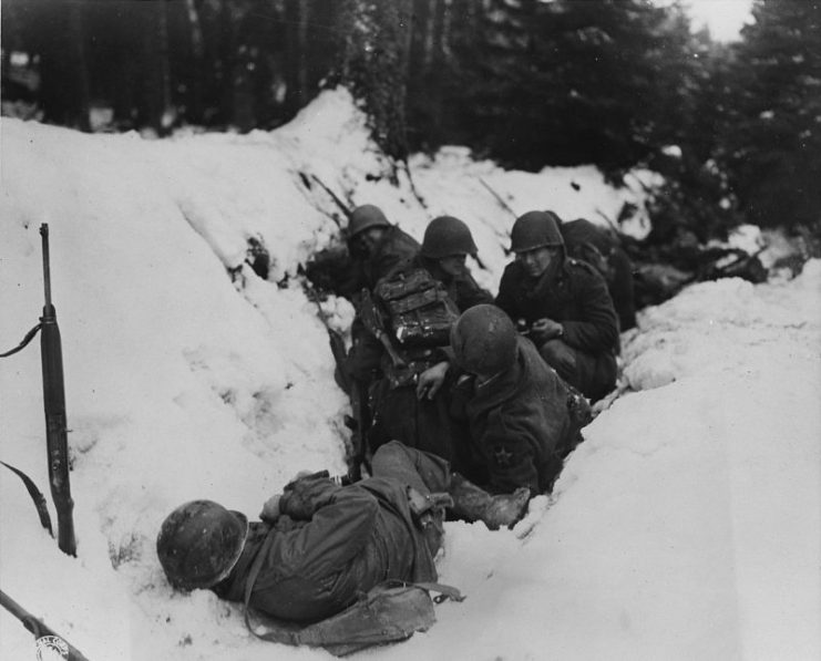 U.S. infantrymen of the 9th Infantry Regiment, 2nd Infantry Division, First U.S. Army, crouch in a snow-filled ditch, taking shelter from a German artillery barrage during the Battle of Heartbreak Crossroads in the Krinkelter woods on 14 December 1944.