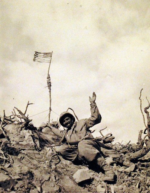Private First Class Edward M. Denellis shown with the flag he carried throughout the campaign to finally place it here atop of a hill during the closing moments of battle
