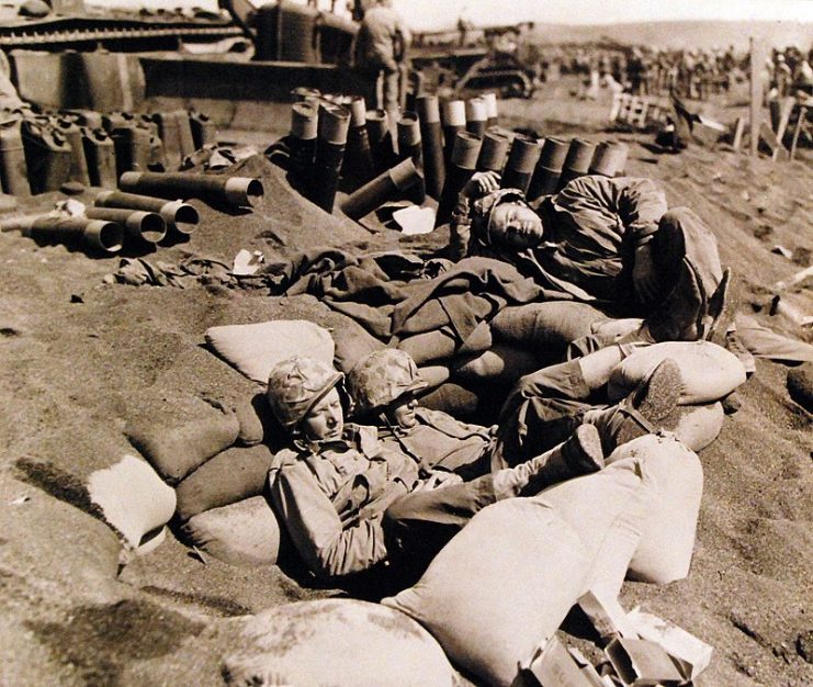 Sprawled in the grey volcanic ash on the beach of Iwo Jima two U.S. Navy Seabees and a Marine seek solace in a quick nap.
