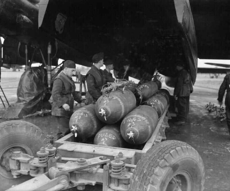 Armourers prepare to load 1,000-lb MC bombs into the bomb-bay of an Avro Lancaster B Mark III of No. 106 Squadron RAF at RAF Metheringham before a major night raid on Frankfurt. The stencilled lettering around the circumference of each bomb reads “RDX/TNT”.