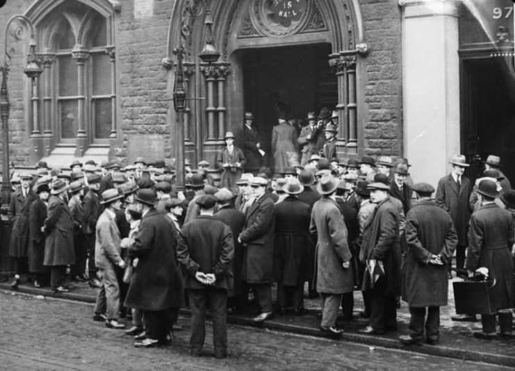Unemployed people in front of a workhouse in London, 1930. By Bundesarchiv – CC BY-SA 3.0 de