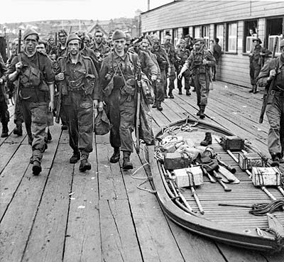 Commandos marching past a collapsed Goatley boat, which was used in smaller raids to transfer from motor boats to the shore