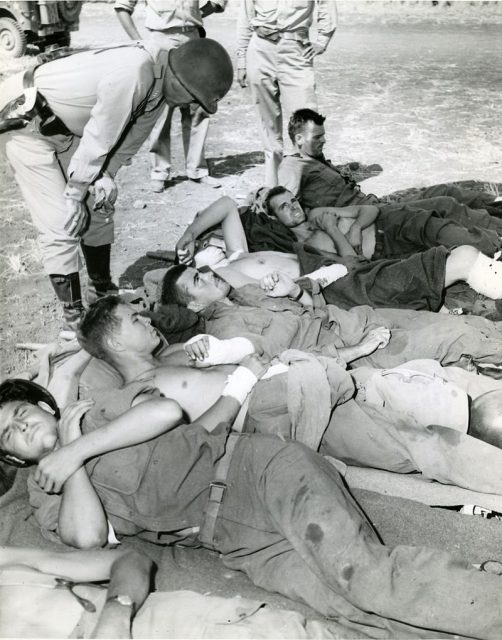 Wounded on Way to Hospital General Patton with Pvt. Frank A. Reed, East Dephon Mass, 7th Infantry 3rd Division suffering from shrapnel wound. Casualties are waiting to be evacuated by air.