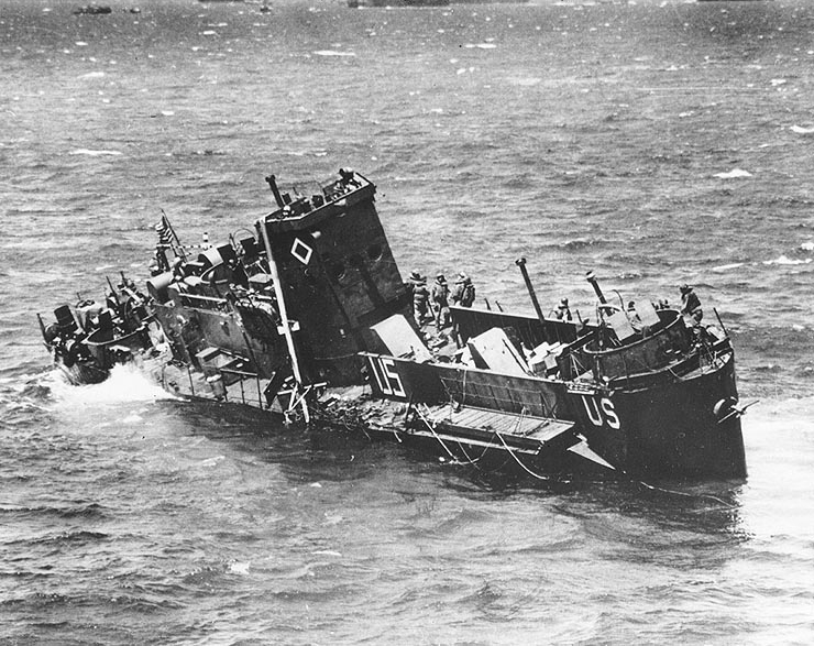A sinking U.S. Coast Guard manned U.S. Navy LCI(L) limps alongside a transport to evacuate her crew, on “D-Day”, 6 June 1944. Wartime censors have painted out the landing craft’s number, but she may be LCI(L)-85, sunk by German shell fire off “Omaha” Beach.