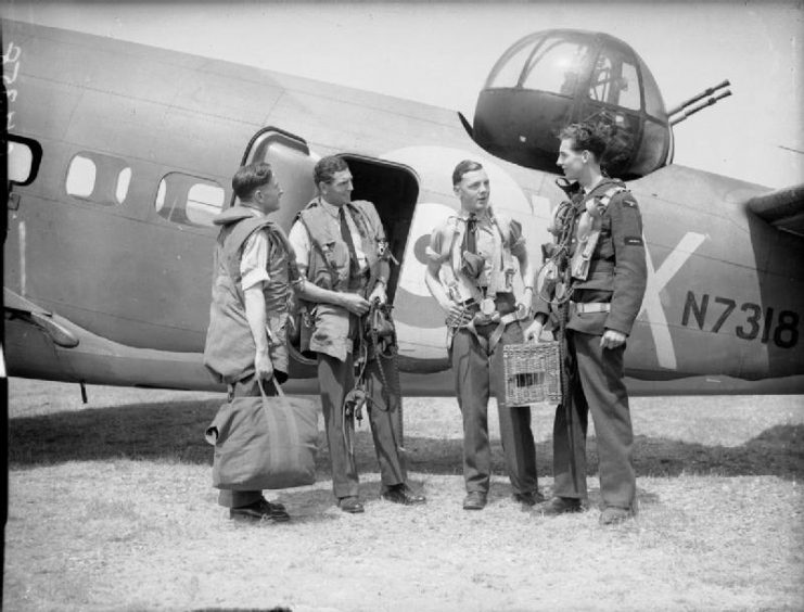 A crew of a Lockheed Hudson Mark holding a wicker carrier containing a homing pigeon.
