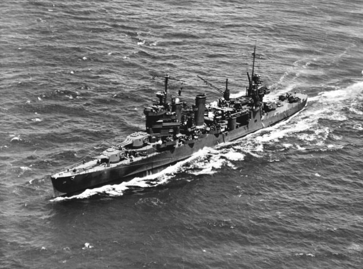 The U.S. Navy heavy cruiser USS Astoria (CA-34) operating in Hawaiian waters during battle practice, 8 July 1942. She appears to be recovering floatplanes from off her starboard side. Note the booms rigged below the forward superstructure to tow aircraft recovery mats, and the starboard crane swung out.