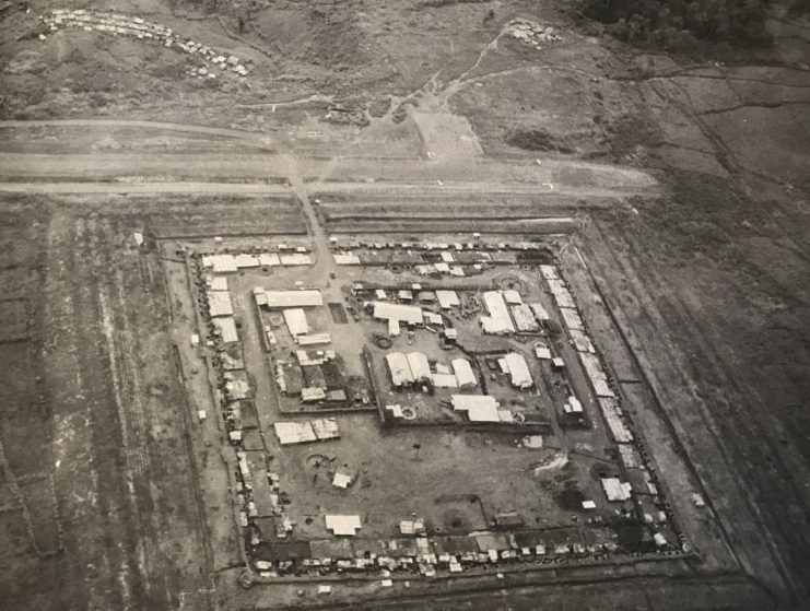 An aerial view of Camp A-245, Dak Seang, in the Central Highlands region of Vietnam. The airstrip is along the top. Rows of barbed and concertina wire surround the camp.