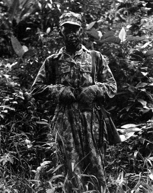An Alamo Scout poses for a photo in full mission attire. He is wearing the M1942 Jungle Suit and is armed with an M1 Carbine. His fatigue cap has been hand-painted to match his Jungle Suit. New Guinea, January 1944.