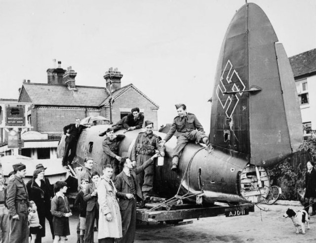 Soldiers collecting for the Spitfire Fund use the fuselage of a Heinkel He 111 as a focus of interest for locals in a street ‘somewhere in south east England’, 10 October 1940.