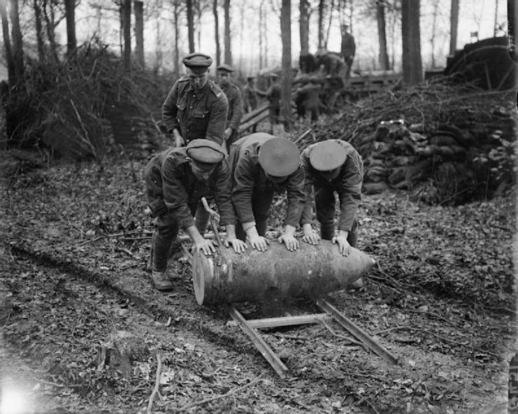 Men of the Royal Garrison Artillery in Englebelmer Wood moving a 15-inch Howitzer shell by rolling it along a pair of rails.