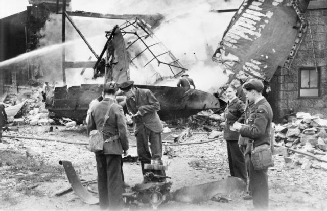 Civilians and RAF airmen inspect the burning remains of a Heinkel He 111 which was shot down by RAF fighters over the north east coast of Scotland and crashed on a house, July 1940.