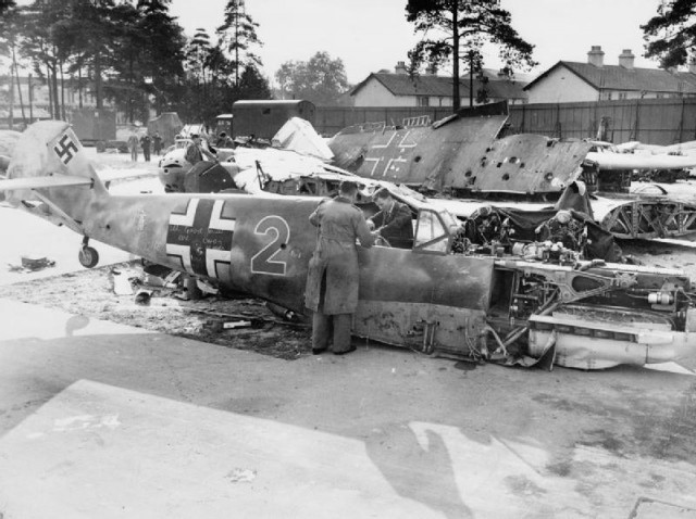Civilian staff investigate the fuselage of a Messerschmitt Bf 109E4, ‘Red 2’, of 3./LG 2, in the grounds of a technical college, 1940. Note the ‘Mickey Mouse’ staffel emblem on the rear fuselage.